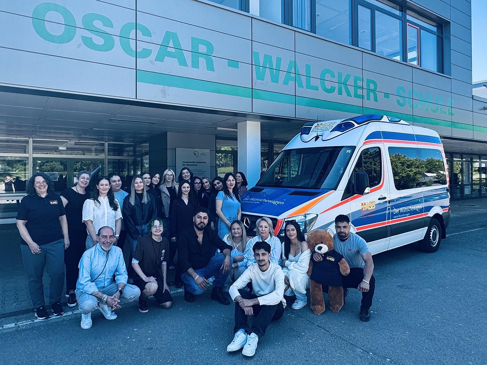 Gruppe von Auszubildenden vor der Oscar-Walcker-Schule neben einem Wünschewagen-Fahrzeug des ASB im Rahmen einer Spendenaktion.
