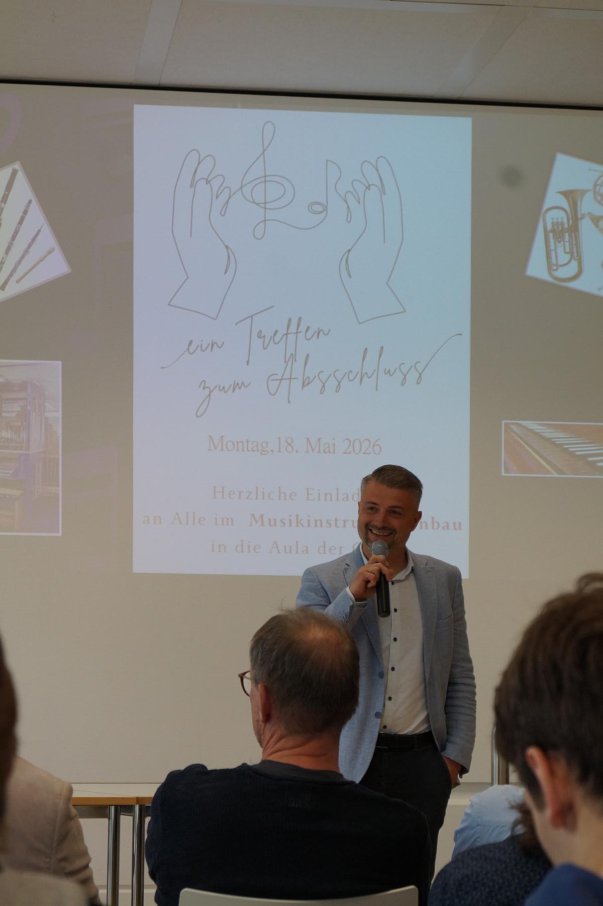 Redebeitrag des stellvertretenden Schulleiters in der Aula der Oscar-Walker-Schule vor projizierter Einladung zur Verabschiedung der Gesellinnen und Gesellen.