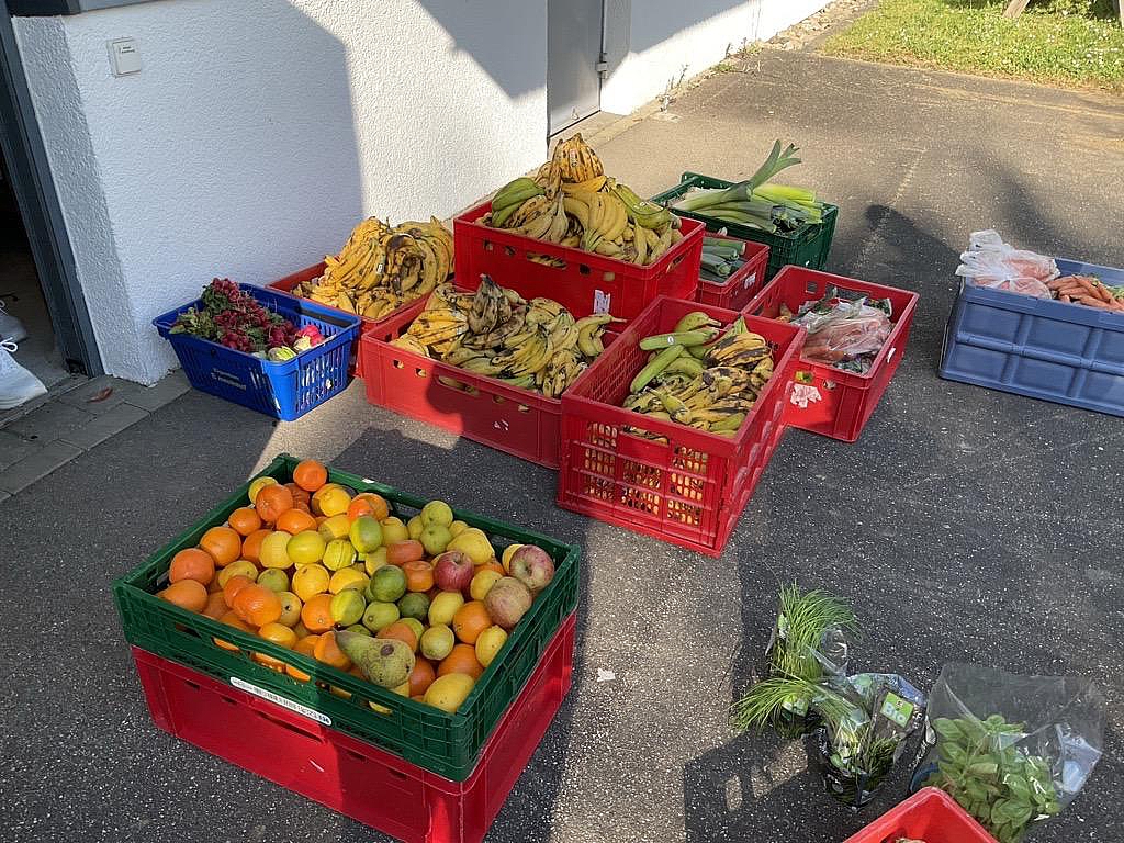 Mehrere Kisten mit geretteten Lebensmitteln wie Bananen, Obst und Gemüse stehen vor dem Schulgebäude zur Weiterverarbeitung bereit.